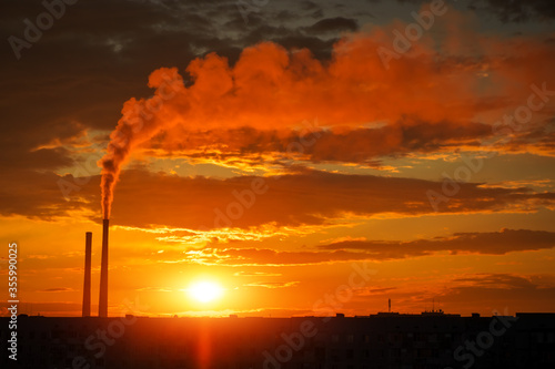 Colorful Magic Sunset. Roofs of city houses during sunrise. Dark smoke coming from the thermal power plant pipe.
