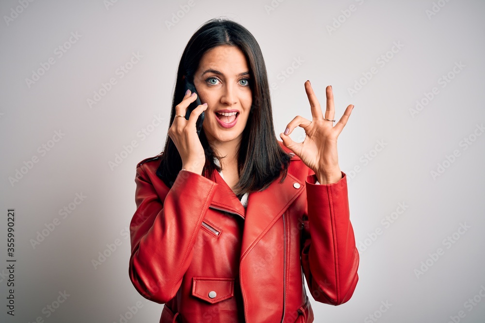 Young brunette woman with blue eyes having a conversation talking on smartphone doing ok sign with fingers, excellent symbol Young brunette woman with blue eyes having a conversation talking on smartphone doing ok sign with fingers, excellent symbol