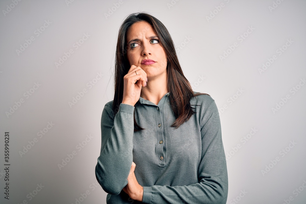 Young brunette woman with blue eyes wearing casual green sweater over white background with hand on chin thinking about question, pensive expression. Smiling with thoughtful face. Doubt concept. Young brunette woman with blue eyes wearing casual green sweater over white background with hand on chin thinking about question, pensive expression. Smiling with thoughtful face. Doubt concept.