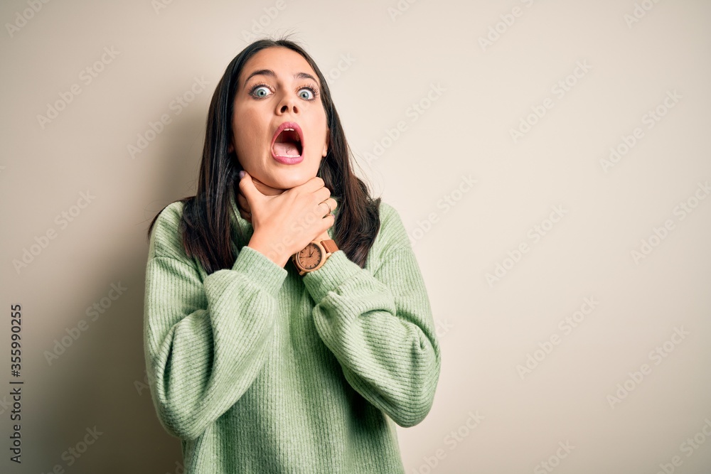 Young brunette woman with blue eyes wearing turtleneck sweater over white background shouting and suffocate because painful strangle. Health problem. Asphyxiate and suicide concept. Young brunette woman with blue eyes wearing turtleneck sweater over white background shouting and suffocate because painful strangle. Health problem. Asphyxiate and suicide concept.