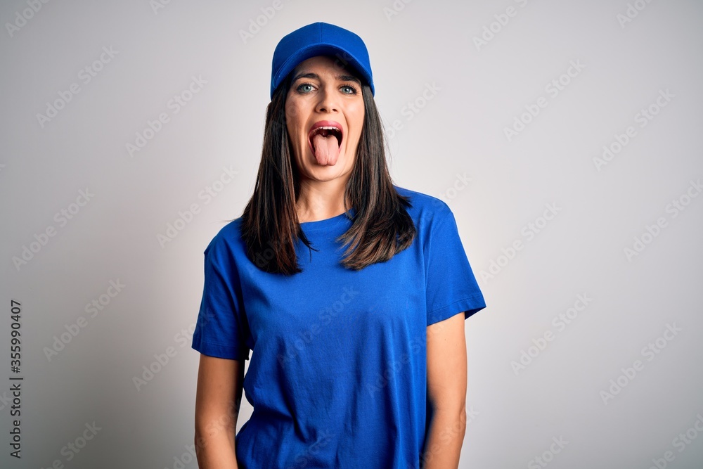 Young delivery woman with blue eyes wearing cap standing over blue background sticking tongue out happy with funny expression. Emotion concept. Young delivery woman with blue eyes wearing cap standing over blue background sticking tongue out happy with funny expression. Emotion concept.