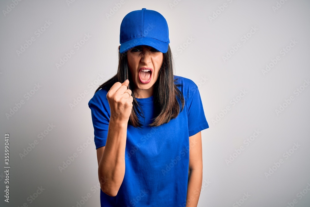 Young delivery woman with blue eyes wearing cap standing over blue background angry and mad raising fist frustrated and furious while shouting with anger. Rage and aggressive concept. Young delivery woman with blue eyes wearing cap standing over blue background angry and mad raising fist frustrated and furious while shouting with anger. Rage and aggressive concept.