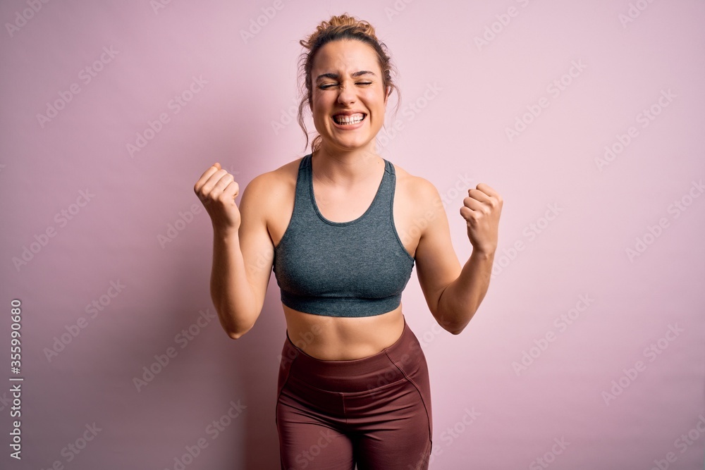 Young beautiful blonde sportswoman doing sport wearing sportswear over pink background excited for success with arms raised and eyes closed celebrating victory smiling. Winner concept.