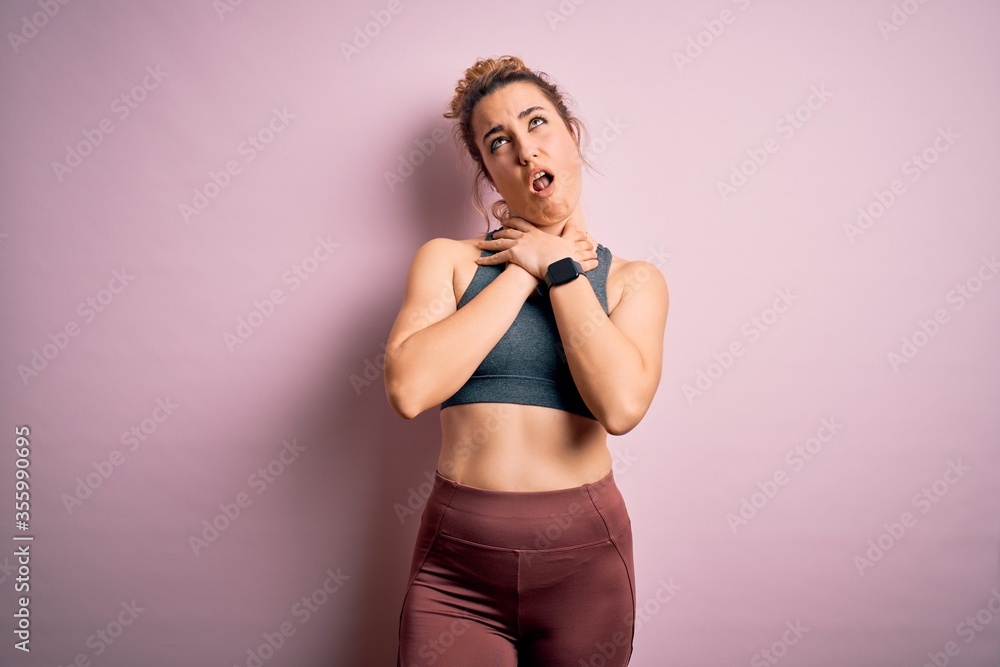 Obraz premium Young beautiful blonde sportswoman doing sport wearing sportswear over pink background shouting suffocate because painful strangle. Health problem. Asphyxiate and suicide concept.