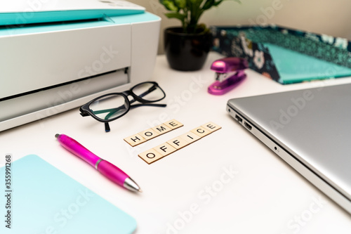 Office desk with laptop, printer, supplies and wooden block letters that say "Home Office". Selective focus