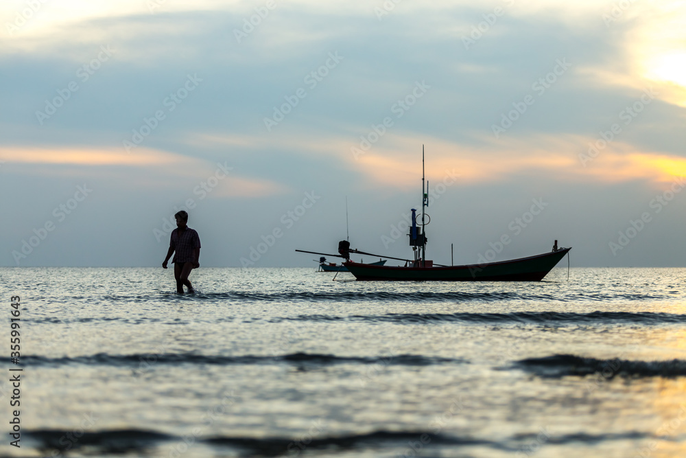 Naklejka premium silhouette of a man walking and fishing Boat in the sea at sunset