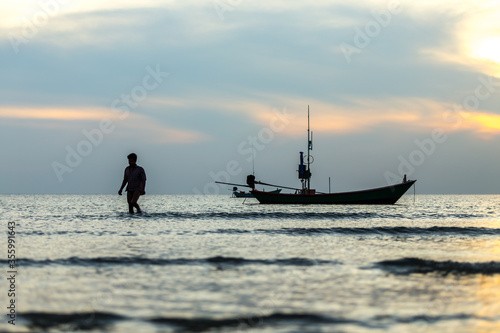 silhouette of a man walking and fishing Boat in the sea at sunset