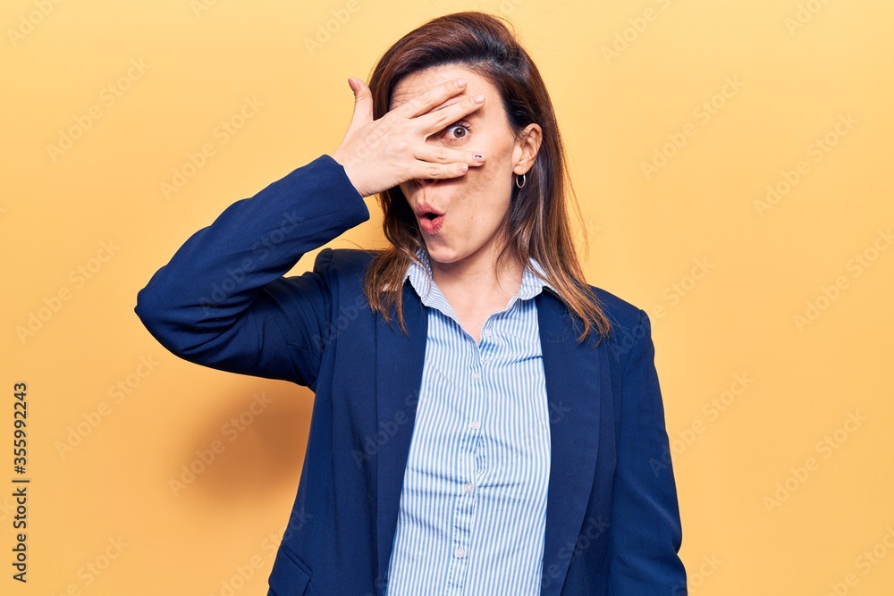 Young beautiful woman wearing business clothes peeking in shock covering face and eyes with hand, looking through fingers afraid Young beautiful woman wearing business clothes peeking in shock covering face and eyes with hand, looking through fingers afraid