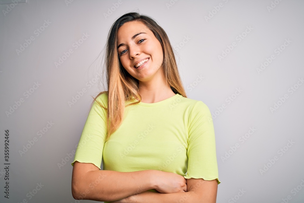 Fototapeta premium Beautiful blonde woman with blue eyes wearing green casual t-shirt over white background happy face smiling with crossed arms looking at the camera. Positive person.
