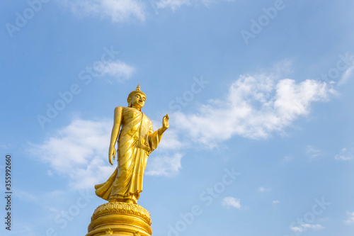 golden standing buddha statue with blue sky in background