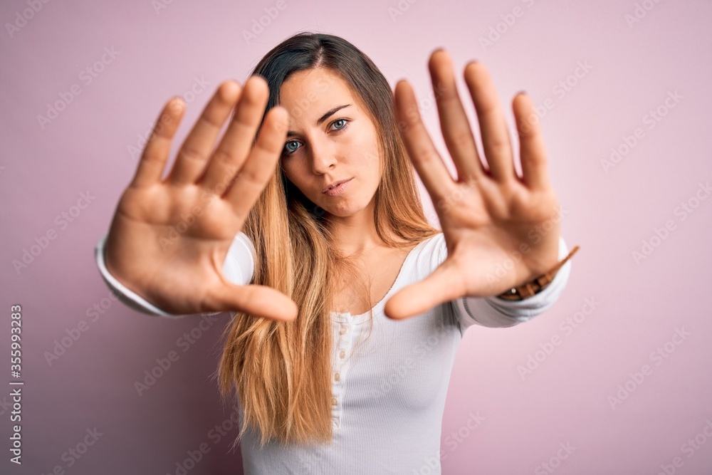 Young beautiful blonde woman with blue eyes wearing white t-shirt over pink background doing frame using hands palms and fingers, camera perspective Young beautiful blonde woman with blue eyes wearing white t-shirt over pink background doing frame using hands palms and fingers, camera perspective