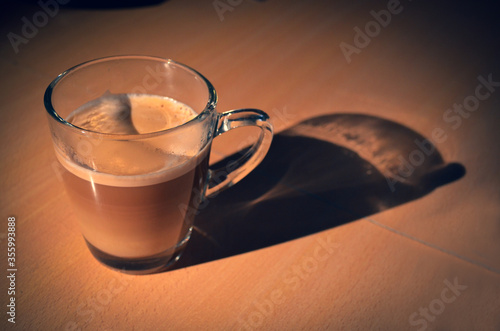 A cup of coffee with milk, over a soft wooden table. Very smooth light pointing to the cup.