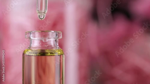 Blend of essential oils closeup. Making some aroma liquids, perfume. Drops falling from pippet to little glass bottle. Slowmotion. Liquid ingredients, body care production, cosmetology. photo