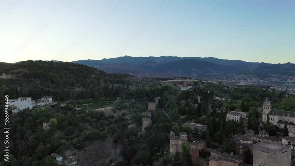 Aerial shot of famous palace amidst trees on hill against sky, drone flying backward from landmark during sunset - Granada, Spain Aerial shot of famous palace amidst trees on hill against sky, drone flying backward from landmark during sunset - Granada, Spain