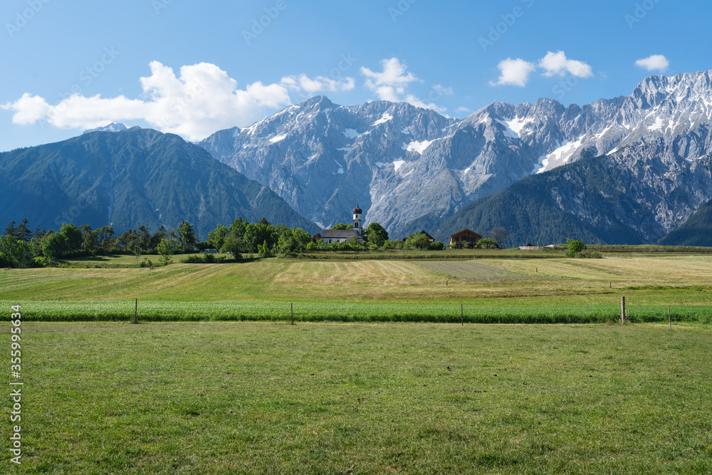 Green meadows along the rocky mountain range with typical small Austrian church, Mieming, Austria