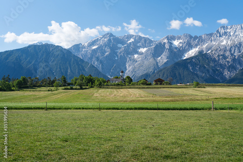 Green meadows along the rocky mountain range with typical small Austrian church, Mieming, Austria