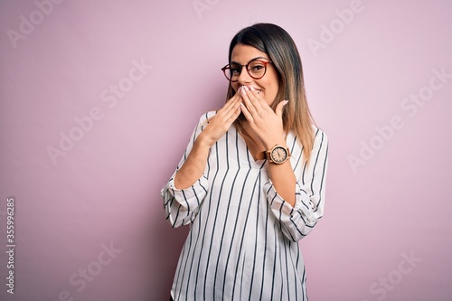Foto Young beautiful woman wearing casual striped t-shirt and glasses over pink backg