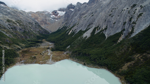 Aerial view of glacier water Emerald Lake in Ushuaia, Tierra del Fuego, Patagonia Argentina. Turquoise water lake in the Andes mountaintop surrounded by rocky mountain peaks and forrest.