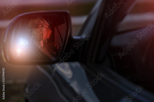 Beautiful girl driver with a mask on her face, sitting at the wheel of the car reflected in the side mirror of the car at night. © Юрий Дровнин