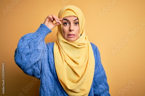 Young beautiful brunette muslim woman wearing arab hijab over isolated yellow background worried and stressed about a problem with hand on forehead, nervous and anxious for crisis © Krakenimages.com