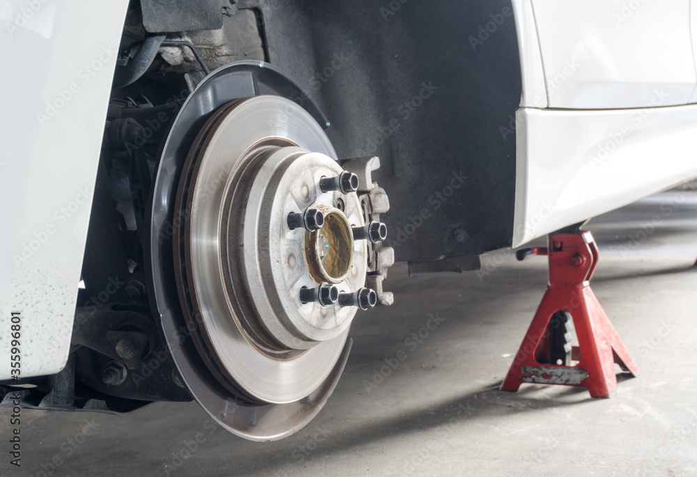 Selective focus of Rear wheel hub and car disk brake ,Car without wheel and lift up by jack stand ( axle stand ), waiting for tire replacement