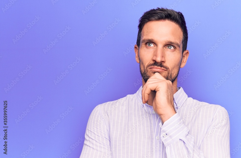 Young handsome man wearing casual striped shirt standing over isolated purple background thinking concentrated about doubt with finger on chin and looking up wondering Young handsome man wearing casual striped shirt standing over isolated purple background thinking concentrated about doubt with finger on chin and looking up wondering