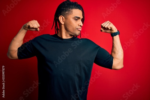 Young handsome african american afro man with dreadlocks wearing casual t-shirt showing arms muscles smiling proud. Fitness concept.