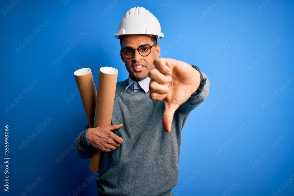 Young african american afro architect man wearing safety helmet holding bluprints with angry face, negative sign showing dislike with thumbs down, rejection concept Young african american afro architect man wearing safety helmet holding bluprints with angry face, negative sign showing dislike with thumbs down, rejection concept