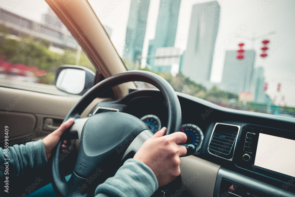 Hands holding steering wheel while driving car on city road Hands holding steering wheel while driving car on city road