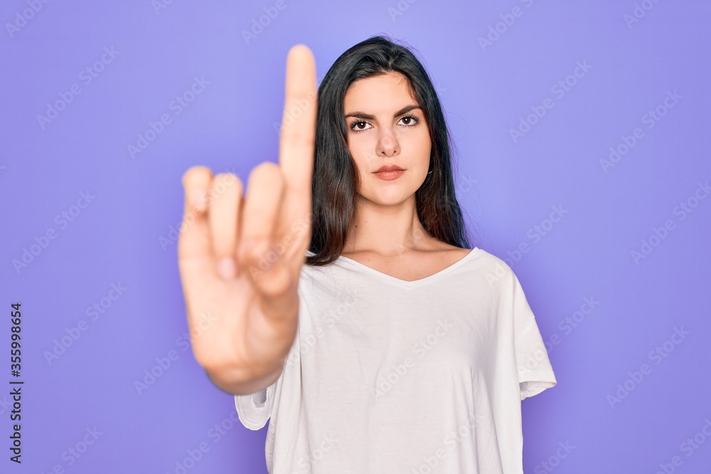 Young beautiful brunette woman wearing casual white t-shirt over purple background Pointing with finger up and angry expression, showing no gesture Young beautiful brunette woman wearing casual white t-shirt over purple background Pointing with finger up and angry expression, showing no gesture