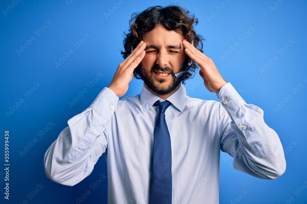 Young handsome call center agent man with beard working using headset over blue background suffering from headache desperate and stressed because pain and migraine. Hands on head. Young handsome call center agent man with beard working using headset over blue background suffering from headache desperate and stressed because pain and migraine. Hands on head.