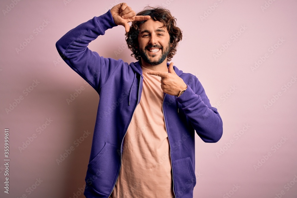 Young handsome sporty man with beard wearing casual sweatshirt over pink background smiling making frame with hands and fingers with happy face. Creativity and photography concept. Young handsome sporty man with beard wearing casual sweatshirt over pink background smiling making frame with hands and fingers with happy face. Creativity and photography concept.