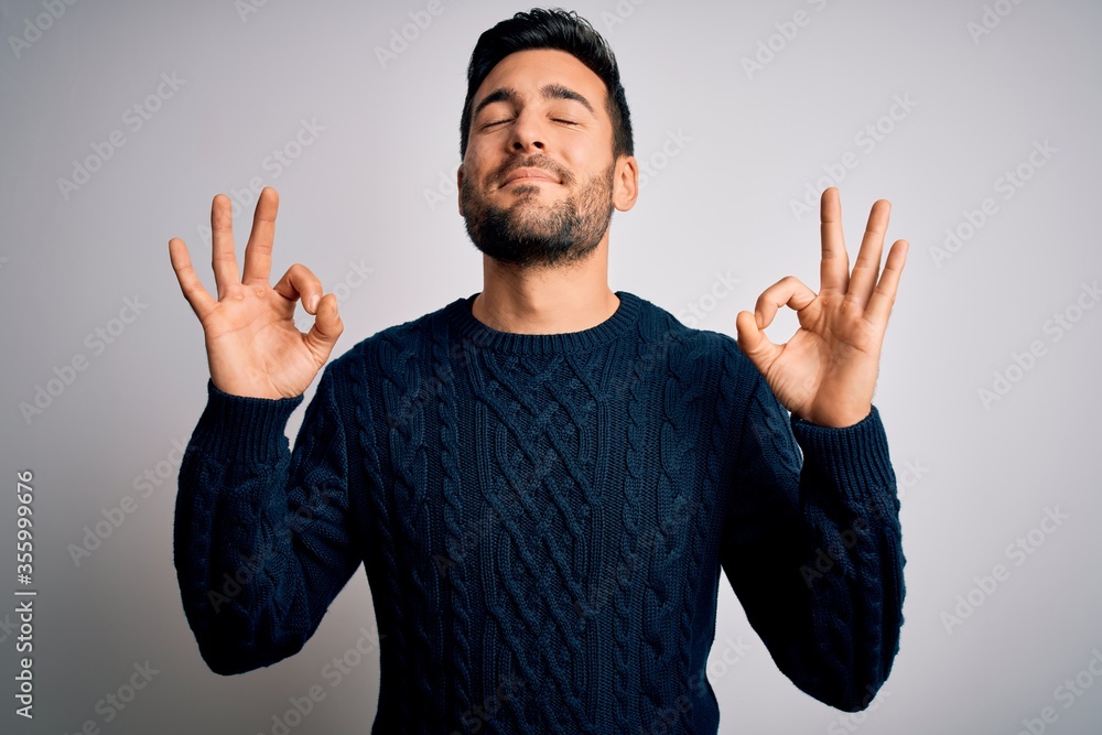 Naklejka premium Young handsome man with beard wearing casual sweater standing over white background relax and smiling with eyes closed doing meditation gesture with fingers. Yoga concept.