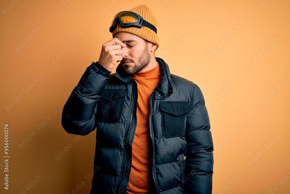 Young handsome skier man with beard wearing snow sportswear and ski goggles tired rubbing nose and eyes feeling fatigue and headache. Stress and frustration concept. Young handsome skier man with beard wearing snow sportswear and ski goggles tired rubbing nose and eyes feeling fatigue and headache. Stress and frustration concept.
