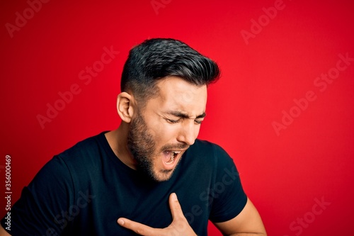 Young handsome man wearing casual black t-shirt standing over isolated red background with hand on stomach because nausea, painful disease feeling unwell. Ache concept. © Krakenimages.com