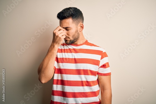 Young handsome man wearing casual striped t-shirt standing over isolated white background tired rubbing nose and eyes feeling fatigue and headache. Stress and frustration concept.