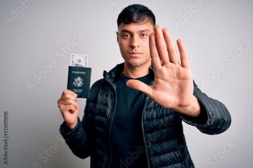 Young hispanic man holding passport document with money over isolated background with open hand doing stop sign with serious and confident expression, defense gesture © Krakenimages.com