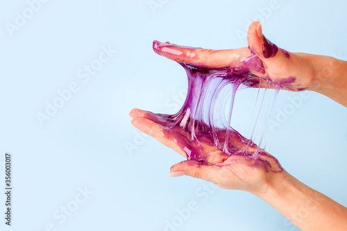 Young girl hands with sticky purple slime on blue background, liquid wax for depilation, conceptual flyer banner with copy space, antistress relax, modern kids hobby oddly satisfying semi surreal asmr photo