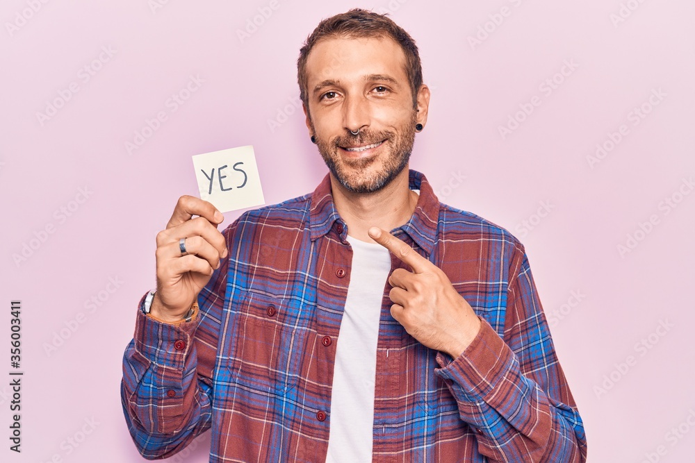 Young handsome man holding yes reminder smiling happy pointing with hand and finger Young handsome man holding yes reminder smiling happy pointing with hand and finger