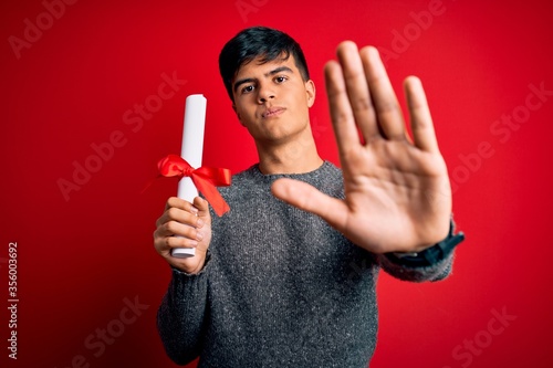 Young student man holding university graduated diploma degree over red background with open hand doing stop sign with serious and confident expression, defense gesture photo