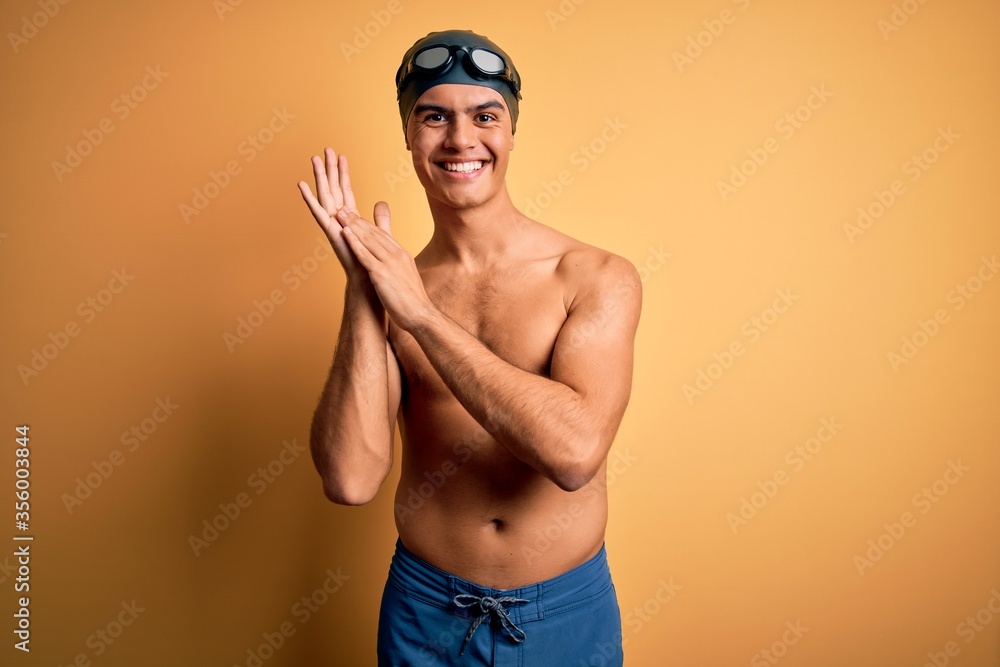 Young handsome man shirtless wearing swimsuit and swim cap over isolated yellow background clapping and applauding happy and joyful, smiling proud hands together