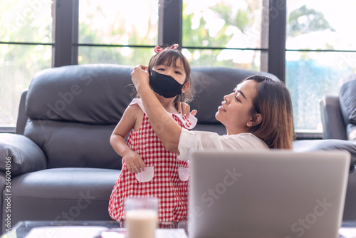 beautiful mother teaches her daughter how to mask save covid-19 in theroom; family happy at home. woman is work from home.