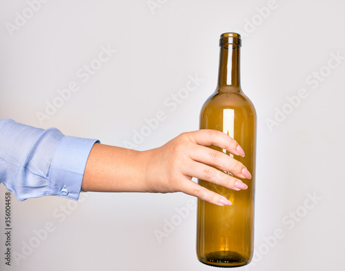 Hand of caucasian young woman holding empty glass botlle of wine over isolated white background