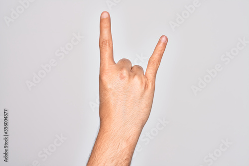 Hand of caucasian young man showing fingers over isolated white background gesturing rock and roll symbol, showing obscene horns gesture