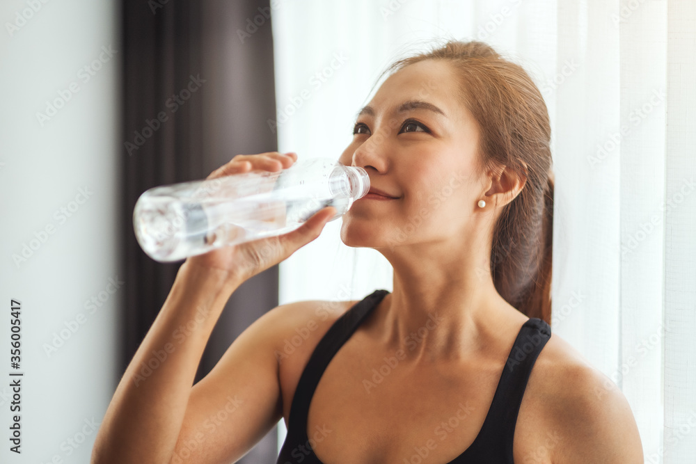 A beautiful asian woman drinking water from plastic bottle while working out A beautiful asian woman drinking water from plastic bottle while working out
