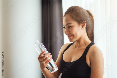 A beautiful asian woman holding and looking at a water bottle while working out