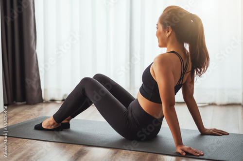 A beautiful young asian woman sitting on training mat and do stretching to warm up before workout at home