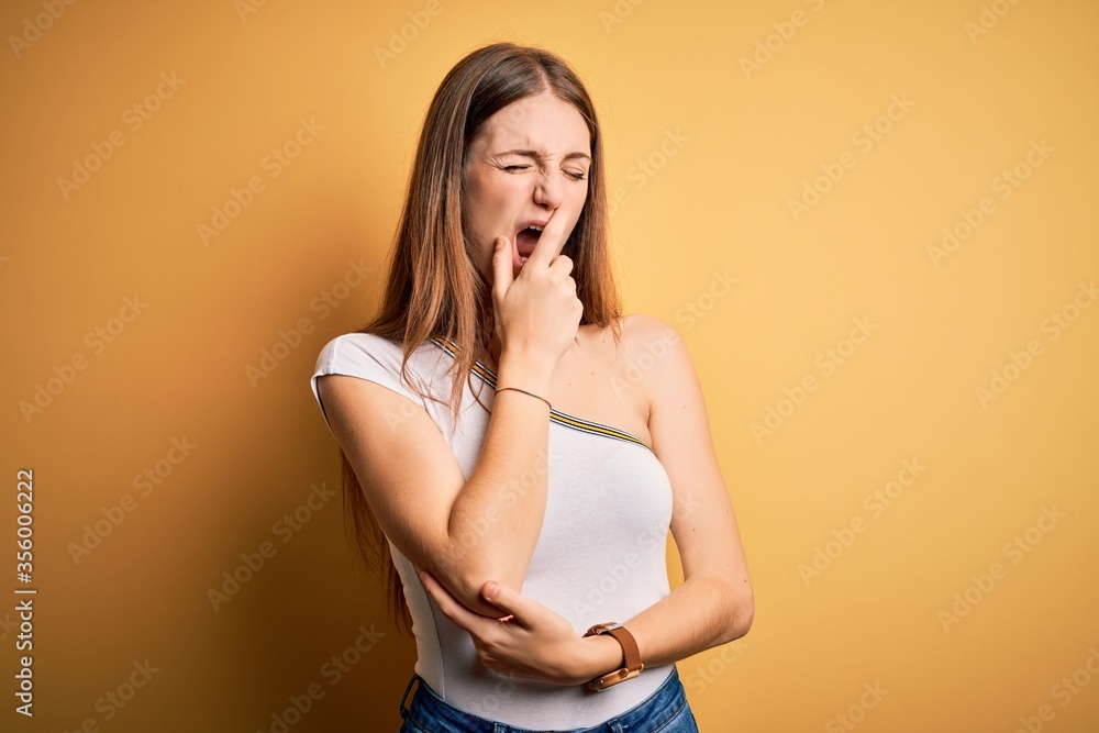 Young beautiful redhead woman wearing casual t-shirt over isolated yellow background bored yawning tired covering mouth with hand. Restless and sleepiness. Young beautiful redhead woman wearing casual t-shirt over isolated yellow background bored yawning tired covering mouth with hand. Restless and sleepiness.