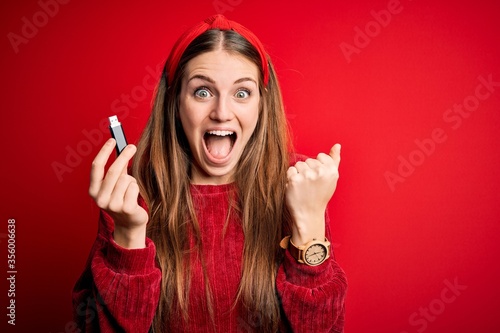 Bilde på lerret Young beautiful redhead woman holding USB memory over isolated red background sc