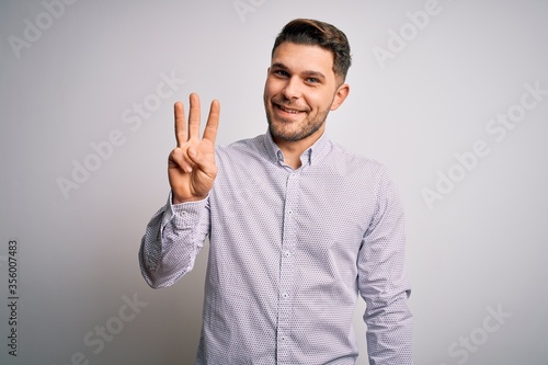 Young business man with blue eyes standing over isolated background showing and pointing up with fingers number three while smiling confident and happy.